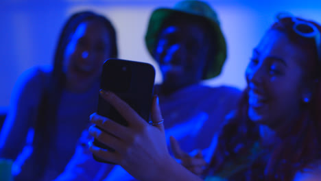 Studio-Shot-Of-Group-Of-Gen-Z-Friends-Sitting-On-Sofa-Posing-For-Selfie-On-Mobile-Phone-At-Night-With-Flashing-Light-4